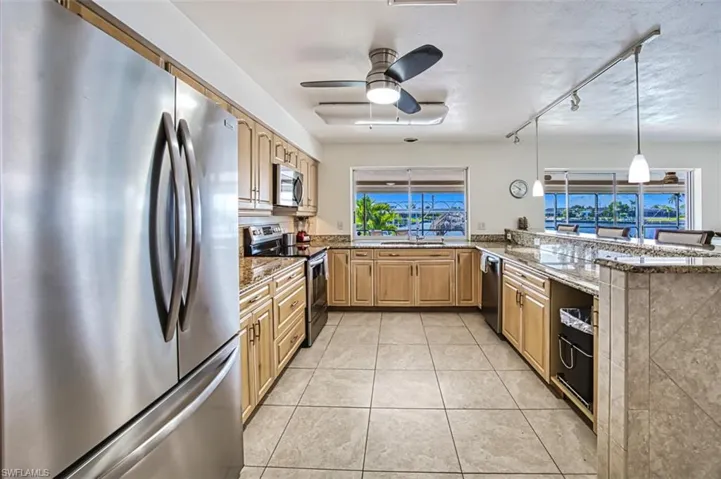 Kitchen with ceiling fan, stone counters, kitchen peninsula, and appliances with stainless steel finishes
