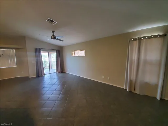 Empty room featuring lofted ceiling, ceiling fan, and dark tile patterned floors