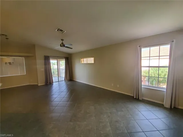 Spare room with plenty of natural light, dark tile patterned floors, a ceiling fan, and vaulted ceiling