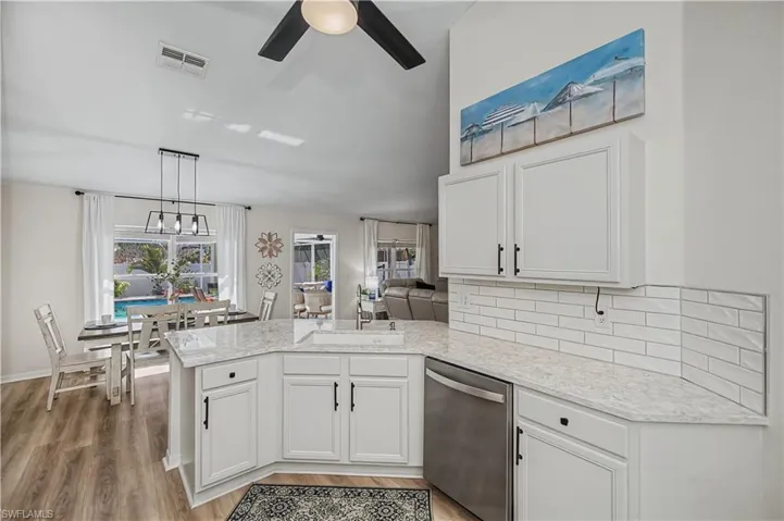 Kitchen featuring a peninsula, white cabinets, stainless steel dishwasher, decorative backsplash, and a ceiling fan