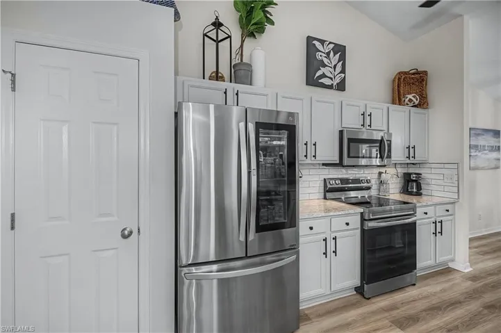 Kitchen with stainless steel appliances, vaulted ceiling, light wood-type flooring, light stone counters, and backsplash