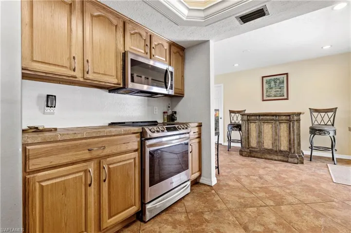 Kitchen featuring stainless steel appliances, a textured ceiling, ornamental molding, and a textured wall
