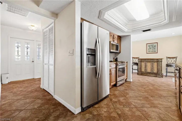 Kitchen featuring stainless steel appliances, ornamental molding, light countertops, light tile patterned flooring, and brown cabinetry
