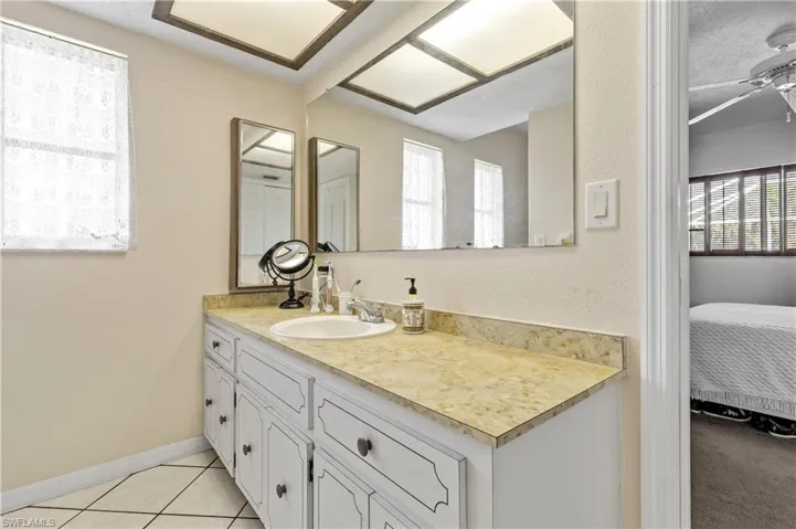 Ensuite bathroom featuring vanity, a textured wall, a textured ceiling, light tile patterned floors, and a ceiling fan