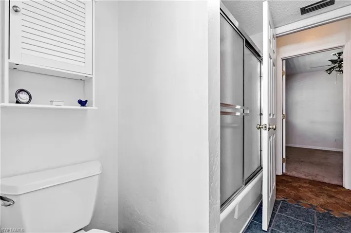 Full bath with bath / shower combo with glass door, a textured ceiling, and dark stone finish flooring