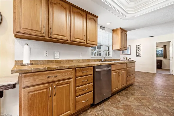 Kitchen featuring stainless steel dishwasher, crown molding, brown cabinetry, and tile countertops