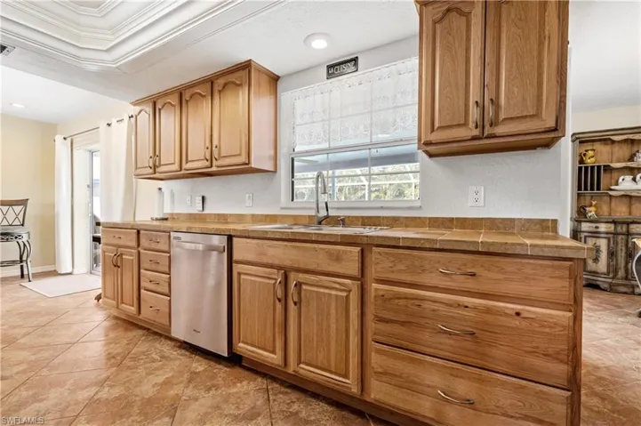 Kitchen featuring dishwasher, ornamental molding, recessed lighting, light tile patterned flooring, and brown cabinetry