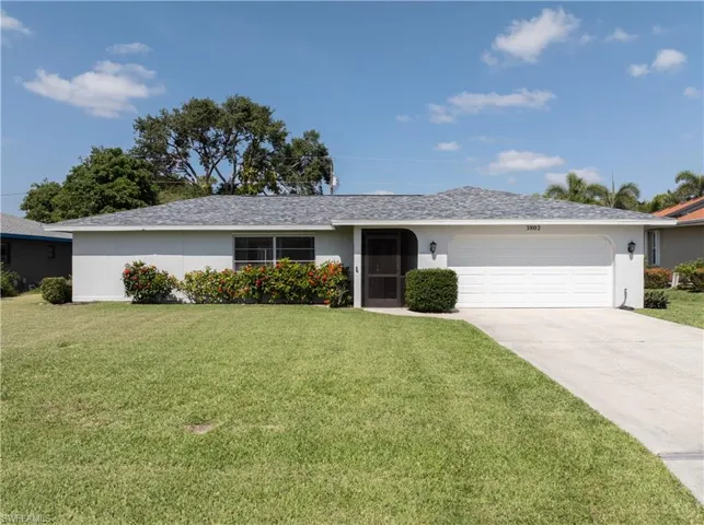 Ranch-style house with a front yard, driveway, a garage, and stucco siding