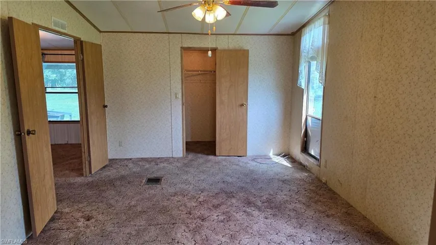 Ceiling fan with light fixture, patterned wallpaper, carpeted flooring, and built-in closet