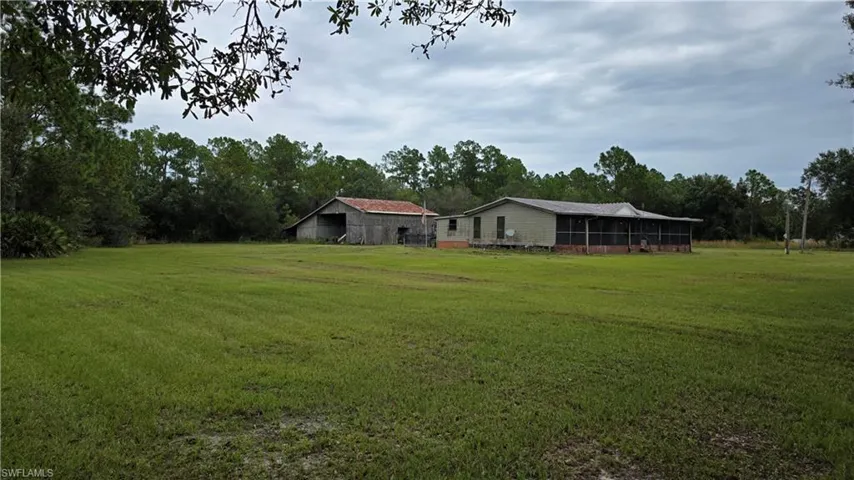 Expansive grassy lot featuring a single-story dwelling, a screened porch, and an outbuilding