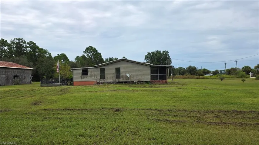 Expansive green lot featuring a single-story dwelling with a screened porch and an adjacent outbuilding
