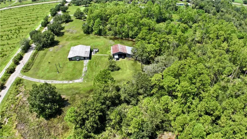 Expansive green space featuring two structures, paved drive, and surrounding mature trees