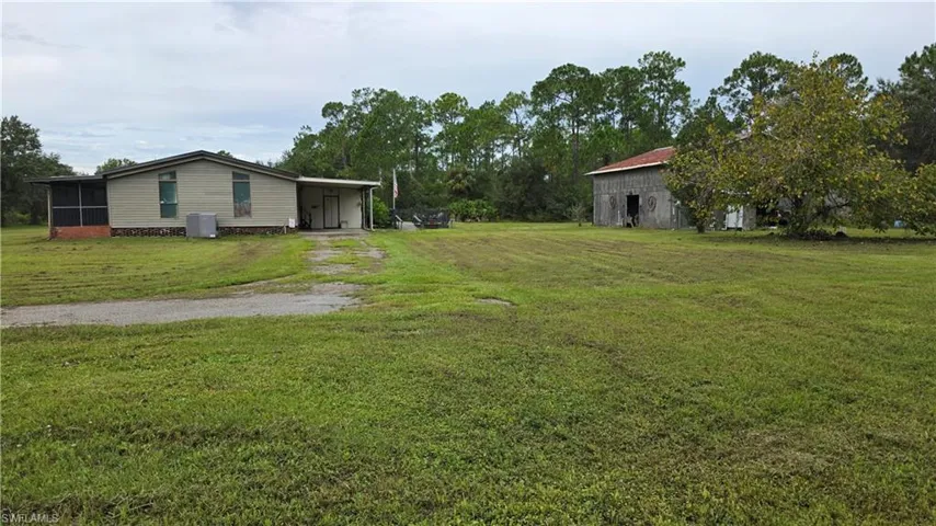 Expansive grassy lot featuring a single-story residence with a screened porch, an attached carport, and an additional detached structure