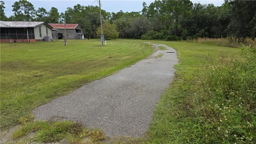 Paved driveway with expansive grassy areas, mature trees, and outbuildings