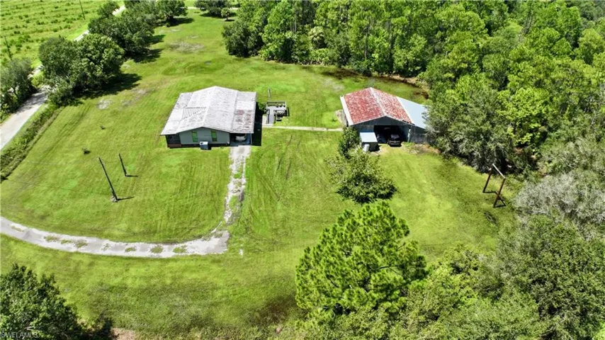 Expansive green acreage featuring a primary dwelling, an additional outbuilding with a metal roof, and surrounding mature trees