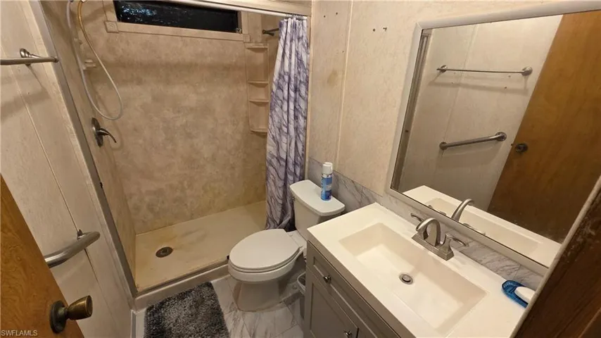 Built-in shower with integrated shelving, vanity with an integrated sink, framed mirror, and toilet