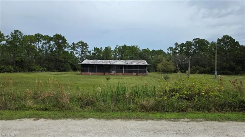 Spacious rural property featuring an open pasture with mature tree line bordering the perimeter and a single-story metal-roof structure positioned on the grounds