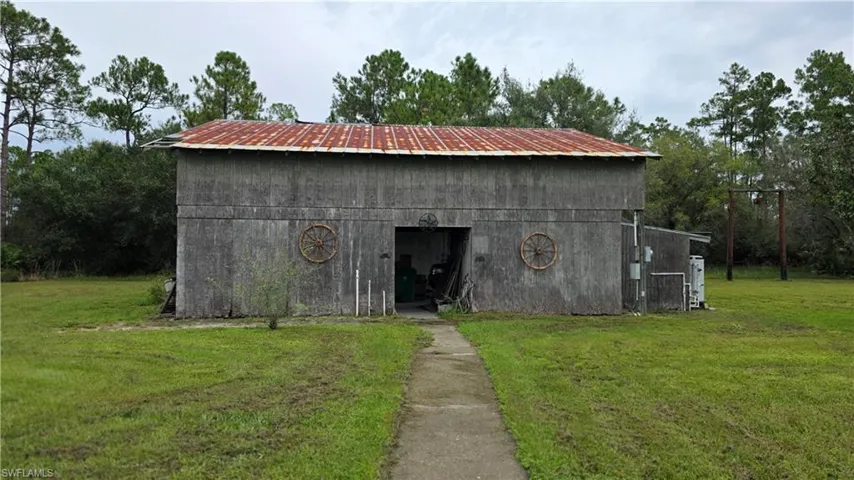 Wood-sided structure with a corrugated metal roof, featuring a concrete pathway and surrounding grassy area
