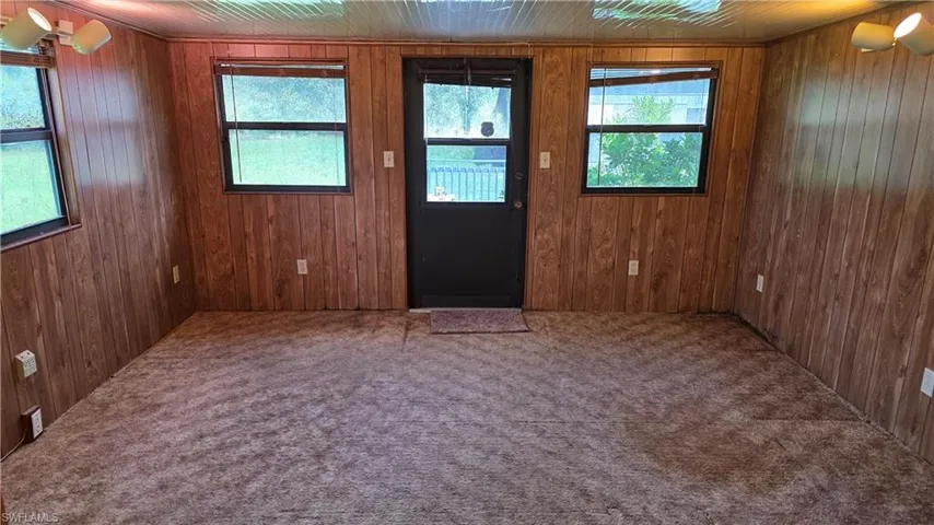 Wood-finish wall paneling, multiple windows, track lighting, and a dark-paneled door