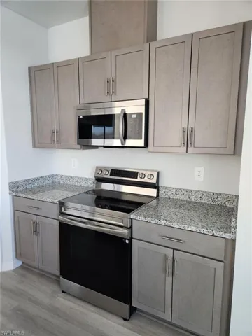 Kitchen with stainless steel appliances, light stone countertops, light wood finished floors, and gray cabinetry