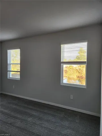 Unfurnished room with dark carpet and baseboards
