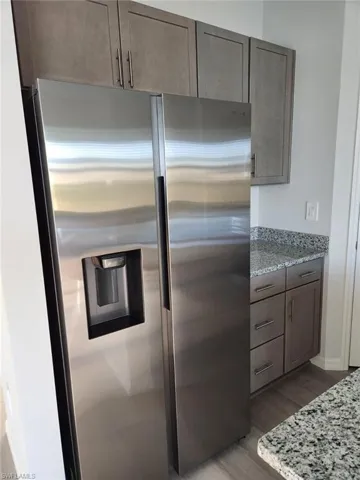Kitchen featuring light stone countertops, stainless steel fridge with ice dispenser, light wood-style floors, and dark wood finish cabinetry