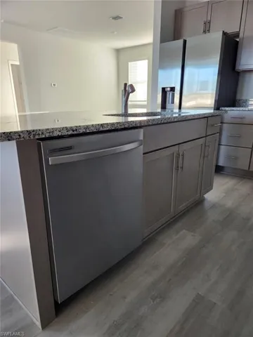 Kitchen featuring stainless steel appliances, dark stone counters, a center island with sink, and light wood-style floors