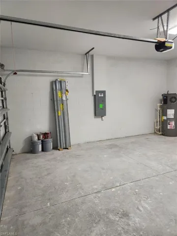 Garage with electric panel, water heater, concrete block wall, and a garage door opener