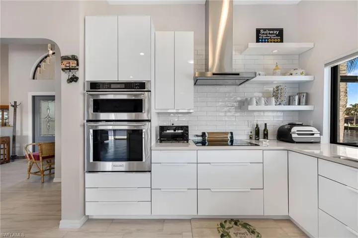 Kitchen with white cabinetry, range hood, black electric cooktop, decorative backsplash, and stainless steel double oven