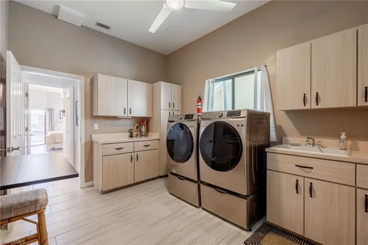 Laundry room with sink, ceiling fan, cabinets, independent washer and dryer, and light wood-type flooring