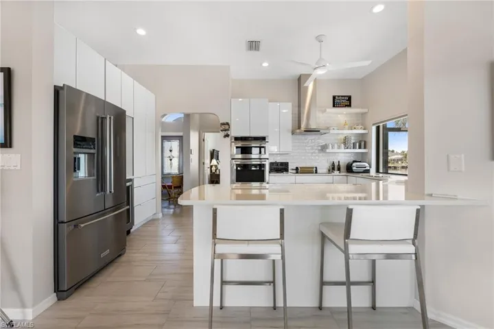Kitchen with a kitchen bar, kitchen peninsula, stainless steel appliances, range hood, and white cabinets