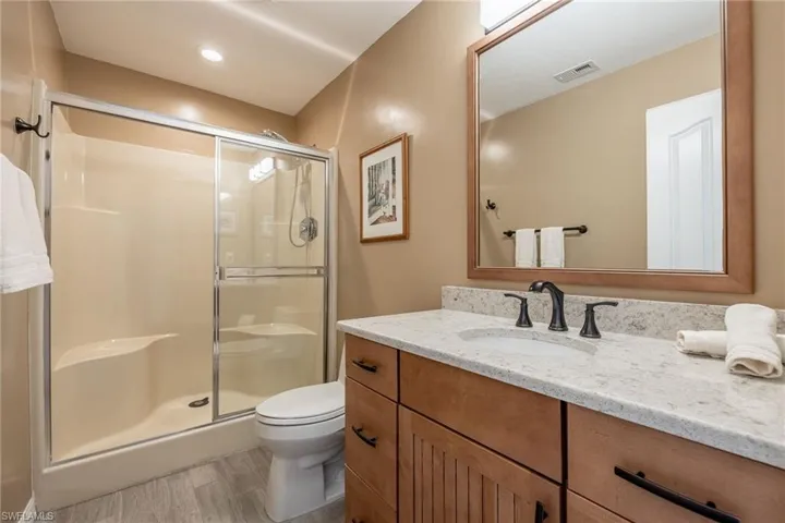 Bathroom featuring vanity, hardwood / wood-style flooring, a shower with shower door, and toilet