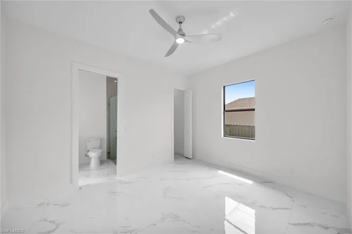 Unfurnished bedroom featuring ceiling fan, ensuite bath, and light tile floors