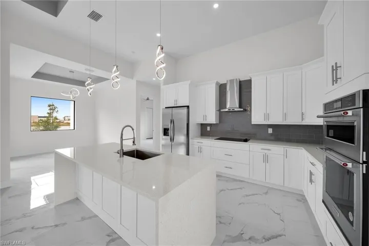 Kitchen with decorative light fixtures, wall chimney range hood, light tile flooring, stainless steel appliances, and backsplash