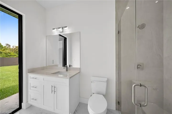 Bathroom with a healthy amount of sunlight, vanity, toilet, and a shower with door