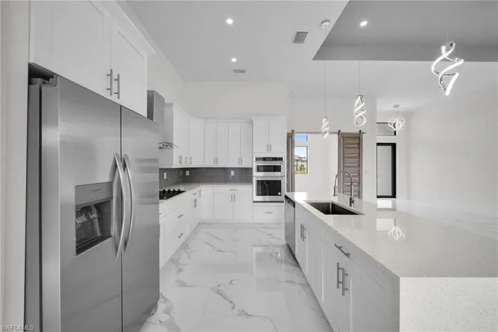 Kitchen featuring wall chimney range hood, appliances with stainless steel finishes, pendant lighting, sink, and light tile flooring