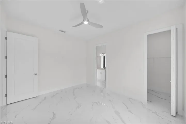 Unfurnished bedroom with ceiling fan, a walk in closet, connected bathroom, and light tile floors