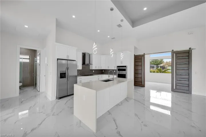 Kitchen with decorative light fixtures, wall chimney range hood, stainless steel appliances, sink, and light tile floors