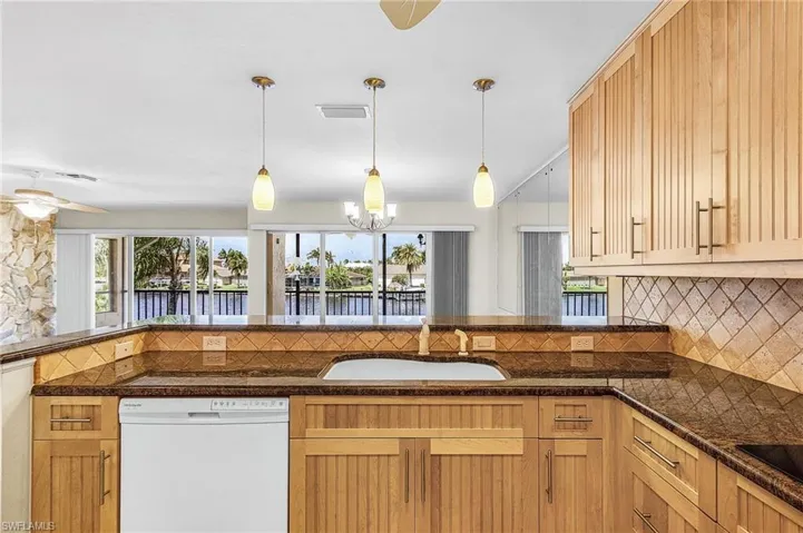 Kitchen featuring white dishwasher, backsplash, a ceiling fan, and hanging light fixtures