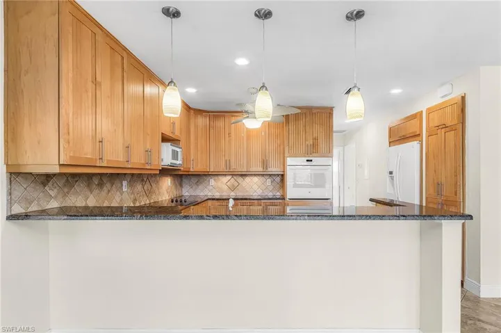 Kitchen featuring dark stone counters, backsplash, a peninsula, hanging light fixtures, and recessed lighting