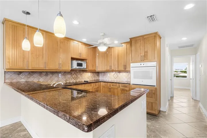 Kitchen featuring white appliances, light tile patterned floors, hanging light fixtures, decorative backsplash, and a peninsula