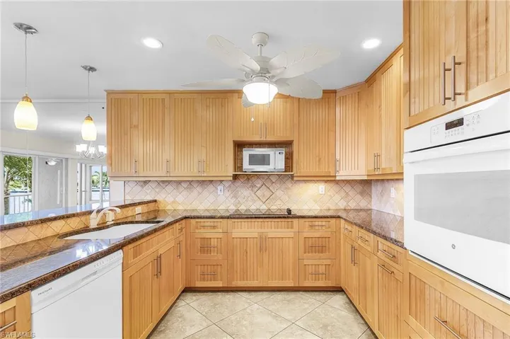 Kitchen with dark stone counters, white appliances, backsplash, decorative light fixtures, and light tile patterned floors