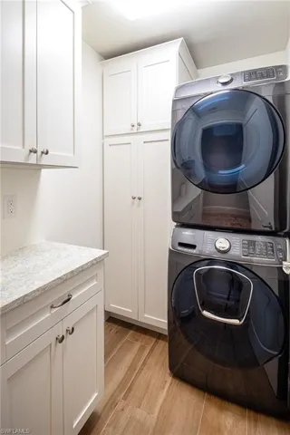 Laundry area with stacked washer and clothes dryer, cabinet space, and light wood-style floors