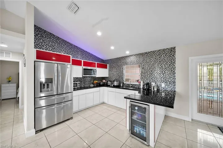 Kitchen with beverage cooler, sink, stainless steel appliances, vaulted ceiling, and white cabinets