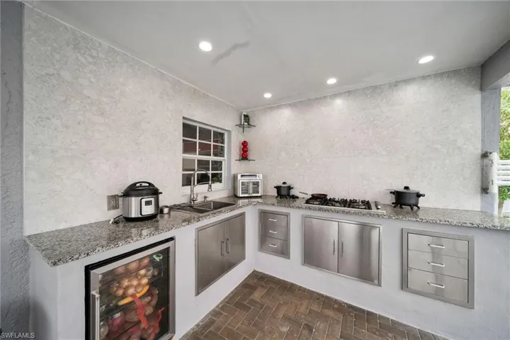 Kitchen with stainless steel gas cooktop, sink, beverage cooler, tile walls, and light stone counters