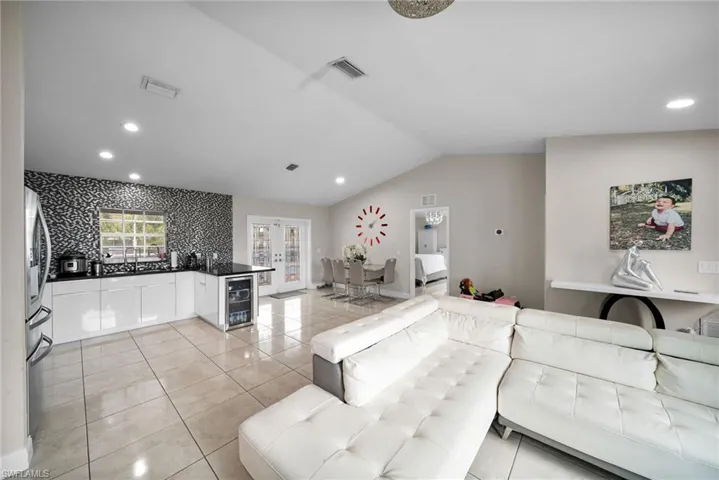 Living room featuring lofted ceiling, french doors, light tile patterned floors, and beverage cooler