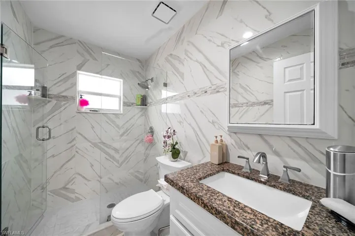 Bathroom with vanity, toilet, tile walls, and a shower with door