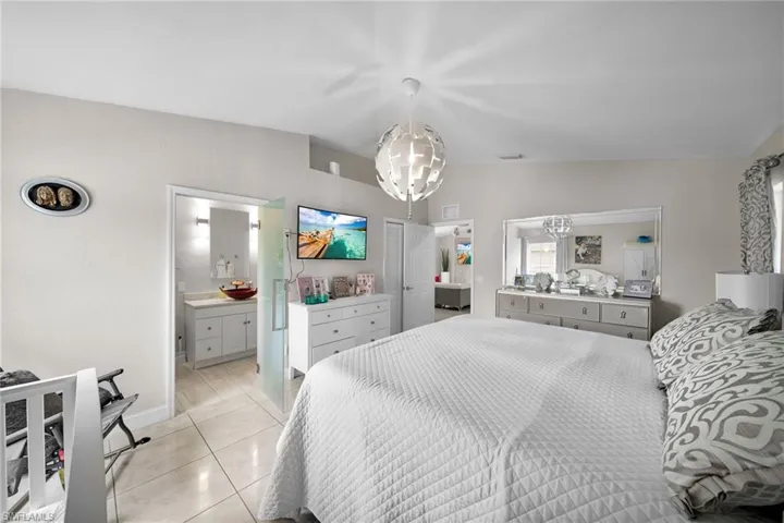 Tiled bedroom with ensuite bath, vaulted ceiling, and a chandelier