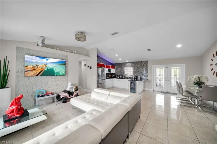 Living room featuring french doors, light tile patterned floors, wine cooler, and vaulted ceiling
