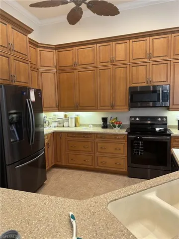 Kitchen featuring crown molding, ceiling fan, light stone countertops, light tile patterned floors, and stainless steel appliances